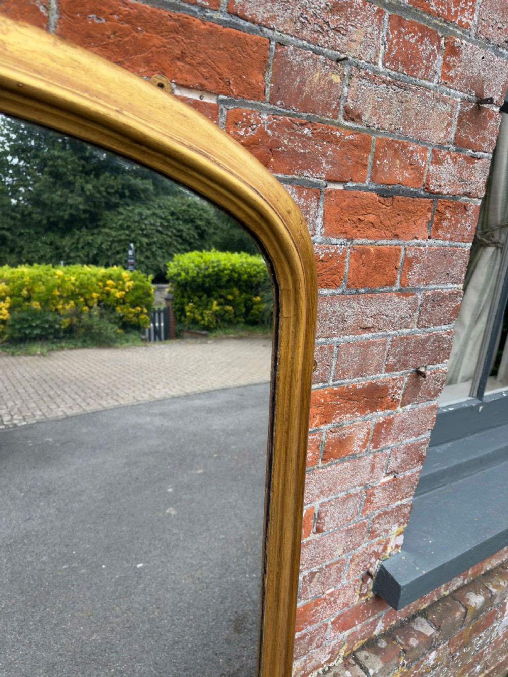 A large 19th-century English overmantel mirror with an arched gold giltwood and gesso frame featuring carved scroll motifs at the base. View VII