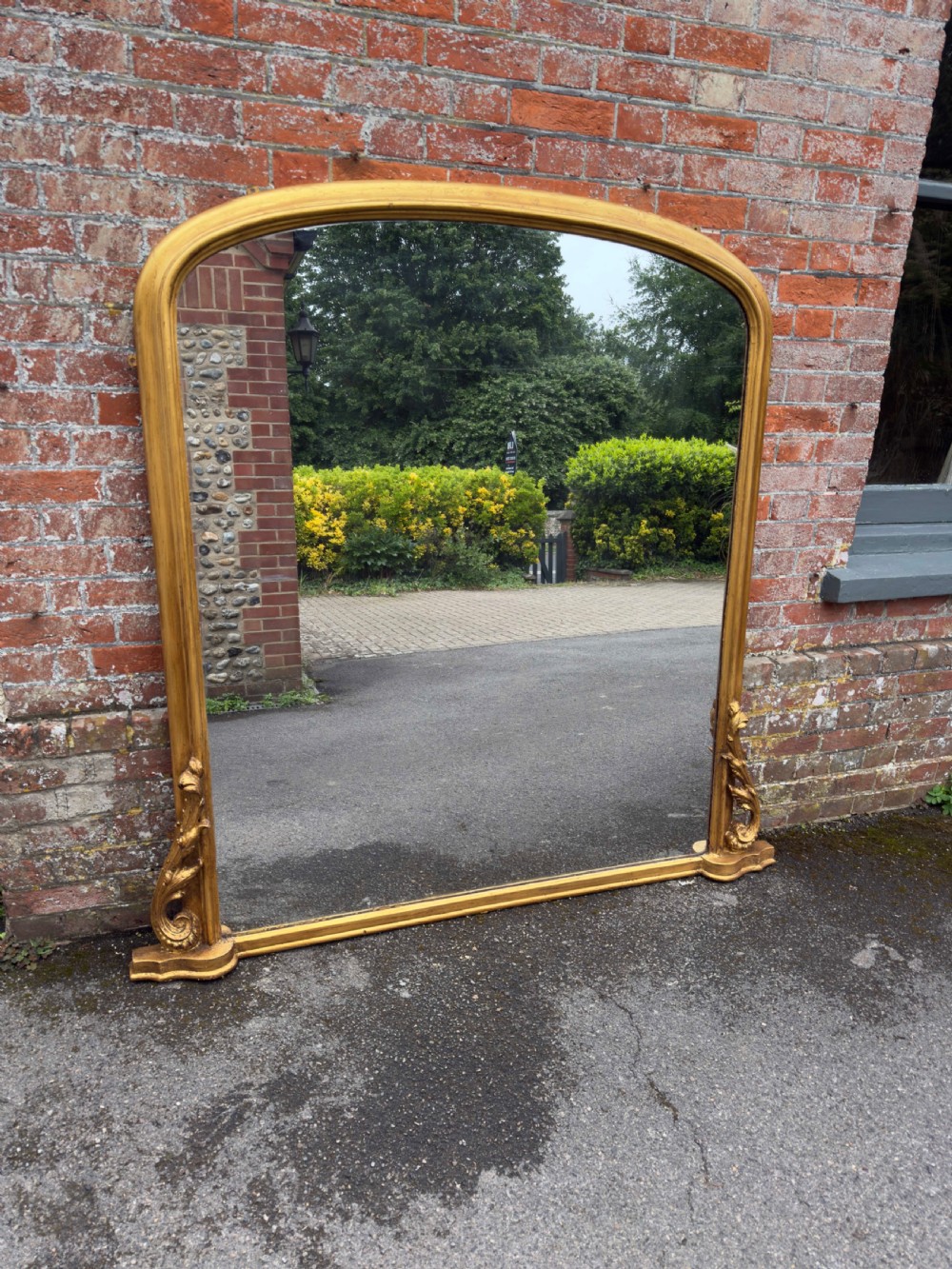 A large 19th-century English overmantel mirror with an arched gold giltwood and gesso frame featuring carved scroll motifs at the base. View VIII
