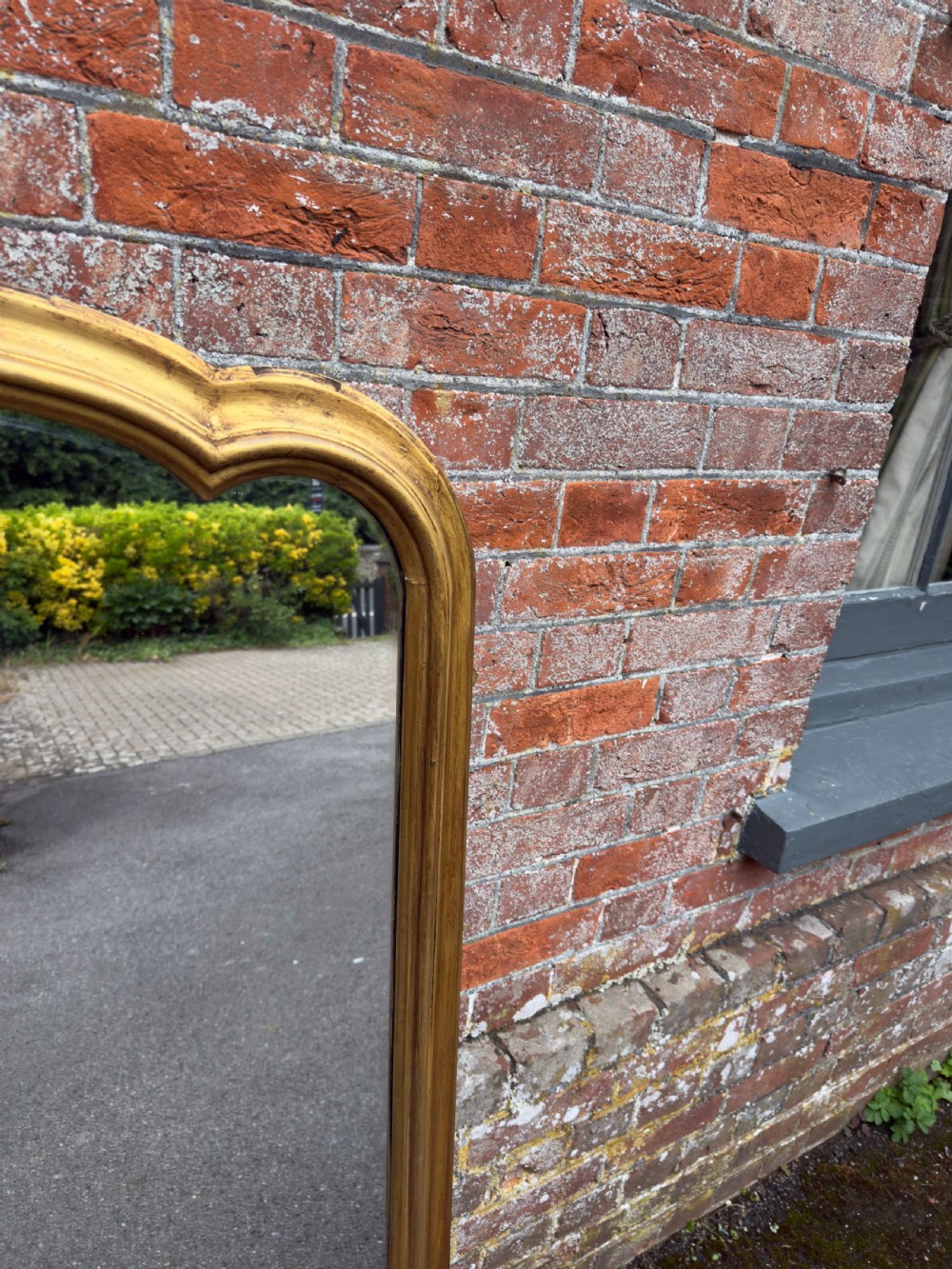A large 19th-century gilded overmantel mirror featuring a shaped upper frame with a carved floral crest and decorative scroll accents at the bottom corners. View III