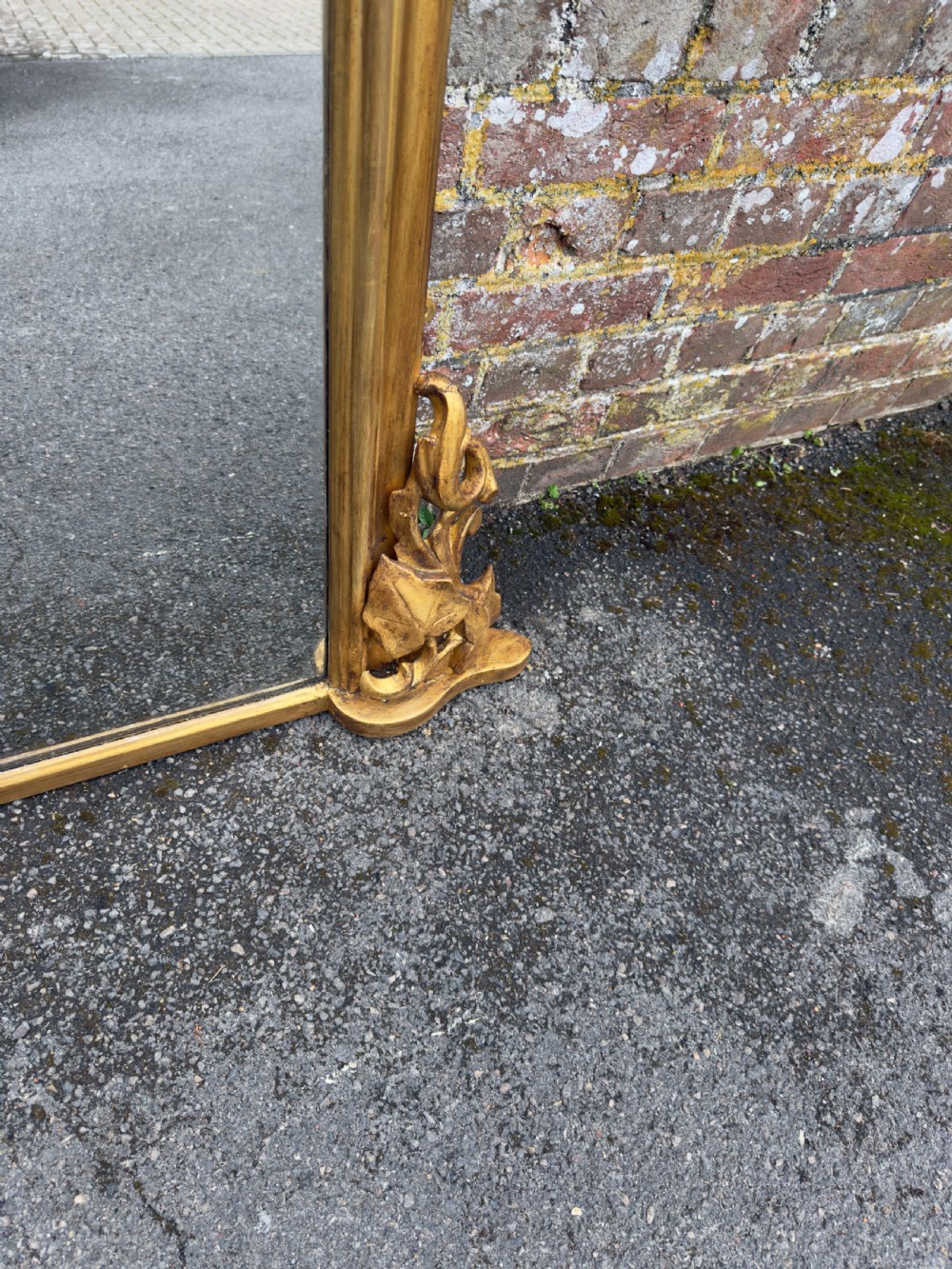 A large 19th-century gilded overmantel mirror featuring a shaped upper frame with a carved floral crest and decorative scroll accents at the bottom corners. View IV