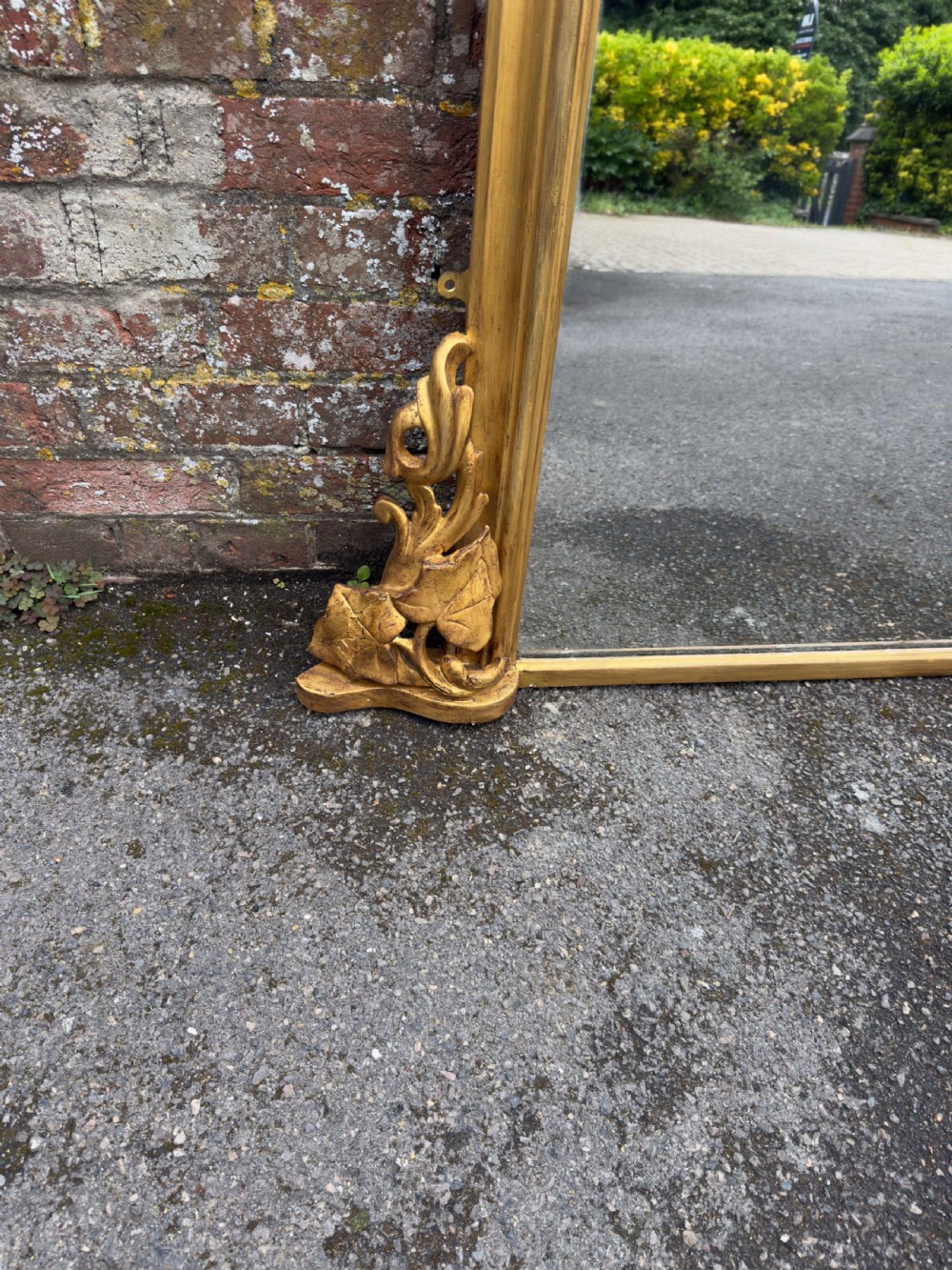 A large 19th-century gilded overmantel mirror featuring a shaped upper frame with a carved floral crest and decorative scroll accents at the bottom corners. View VI