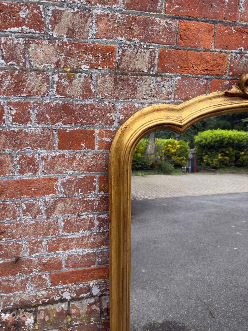 A large 19th-century gilded overmantel mirror featuring a shaped upper frame with a carved floral crest and decorative scroll accents at the bottom corners. View VII