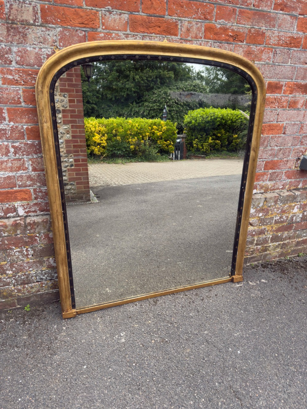A large Victorian arched overmantel mirror featuring a gilded wood frame with a dark inner border detailing.
