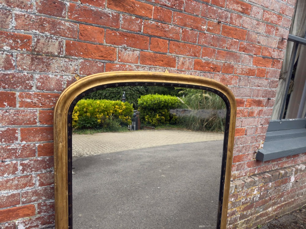 A large Victorian arched overmantel mirror featuring a gilded wood frame with a dark inner border detailing. View II