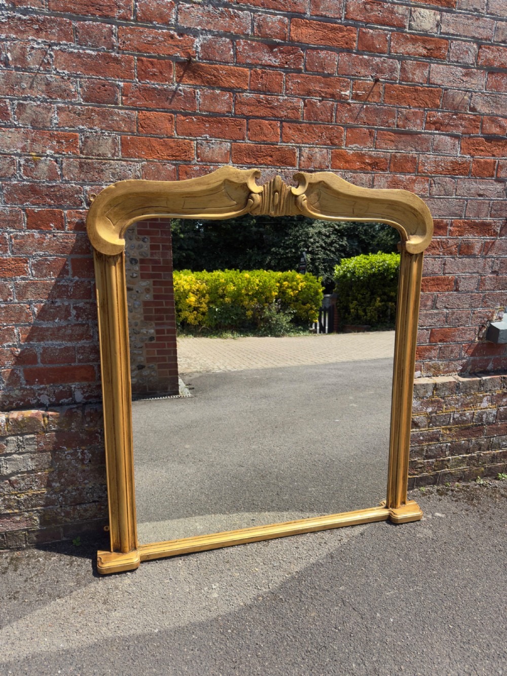 An antique 19th-century English gilt carved wood overmantel mirror featuring a serpentine arched cresting and moulded frame.