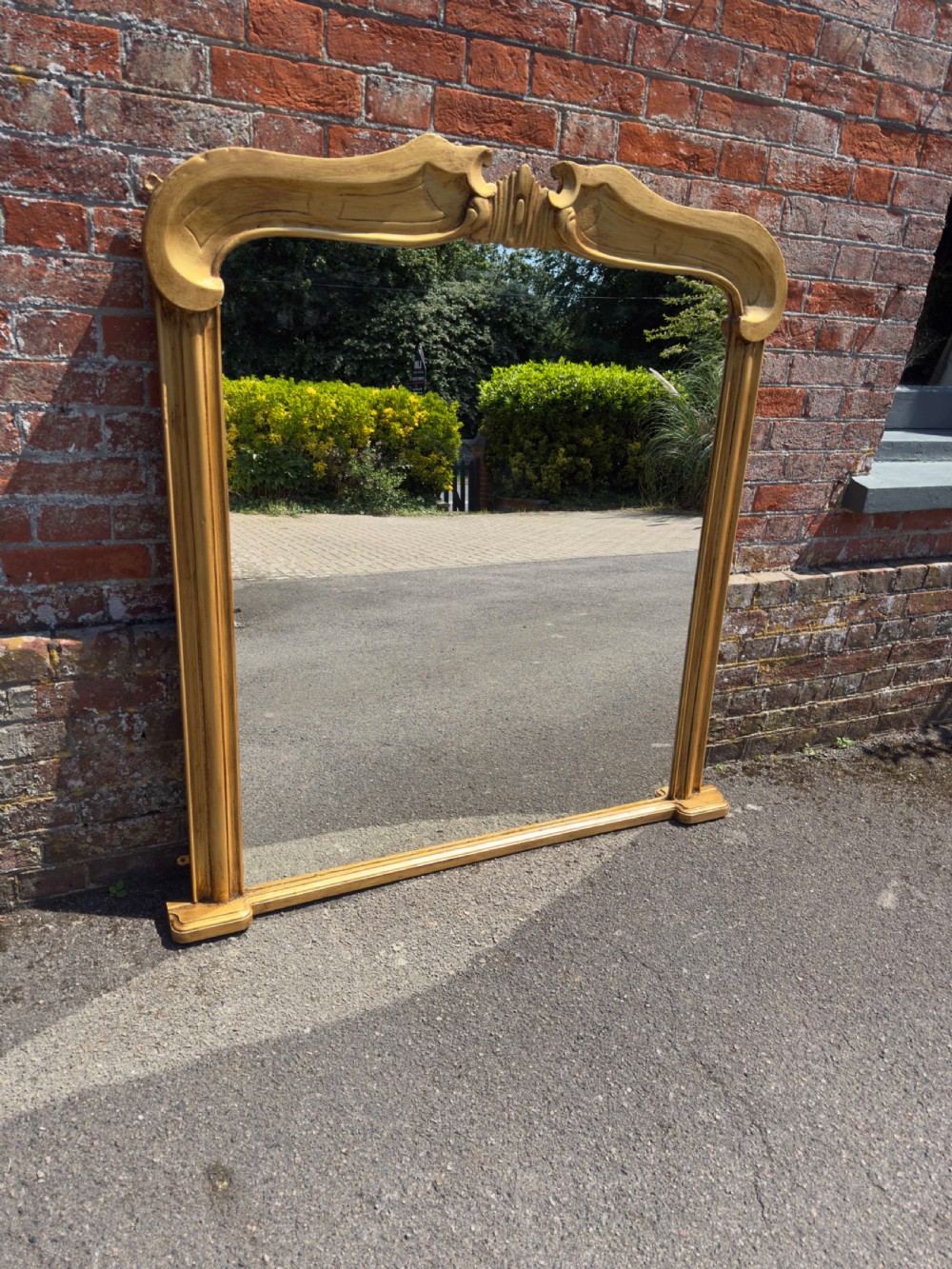 An antique 19th-century English gilt carved wood overmantel mirror featuring a serpentine arched cresting and moulded frame. View VI