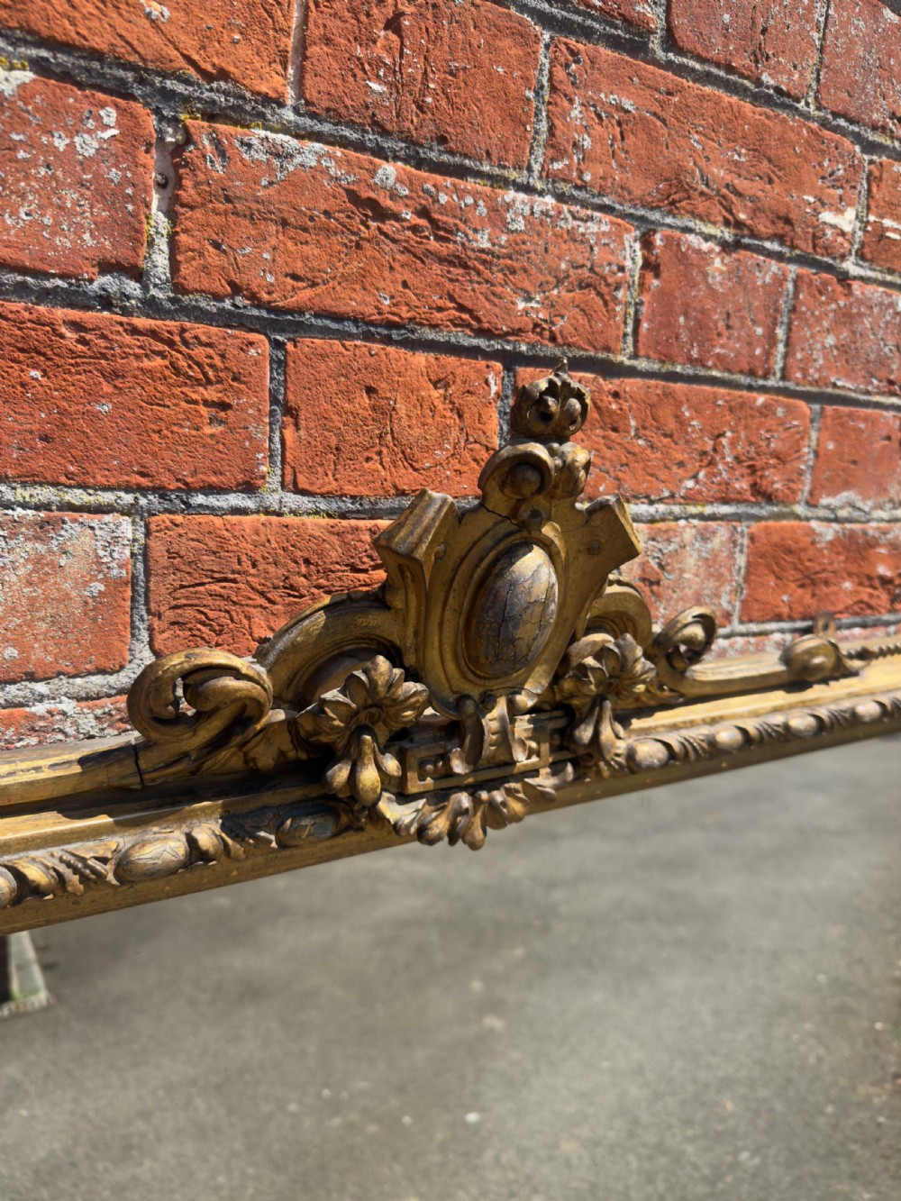 A large 19th-century English giltwood and gesso overmantel mirror featuring an ornate carved central crest, moulded frame, and scrolled side feet. View II