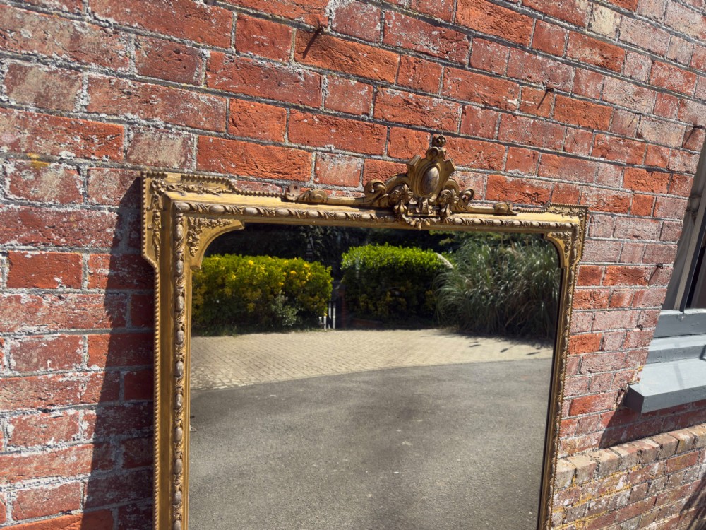 A large 19th-century English giltwood and gesso overmantel mirror featuring an ornate carved central crest, moulded frame, and scrolled side feet. View III