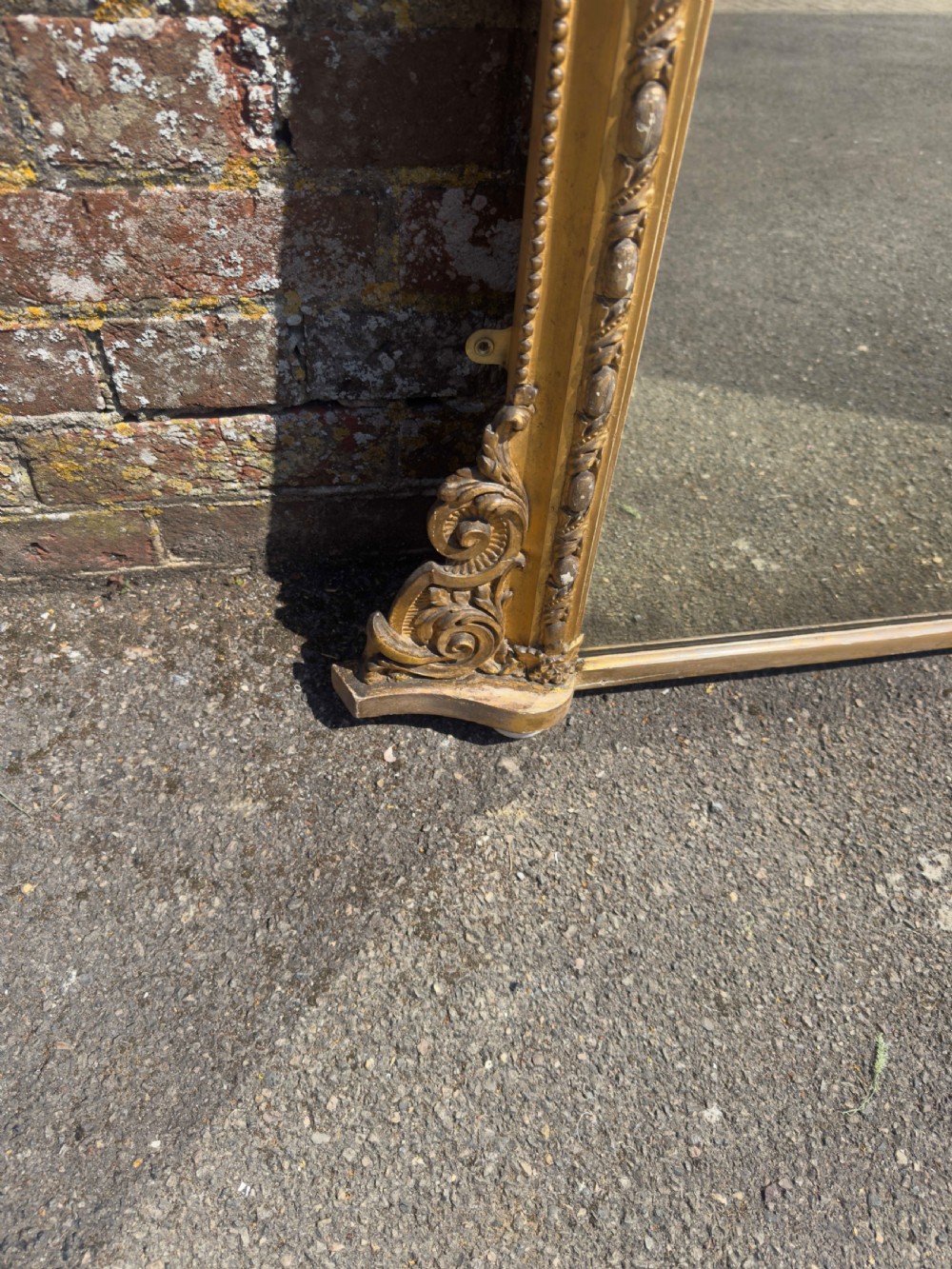 A large 19th-century English giltwood and gesso overmantel mirror featuring an ornate carved central crest, moulded frame, and scrolled side feet. View V