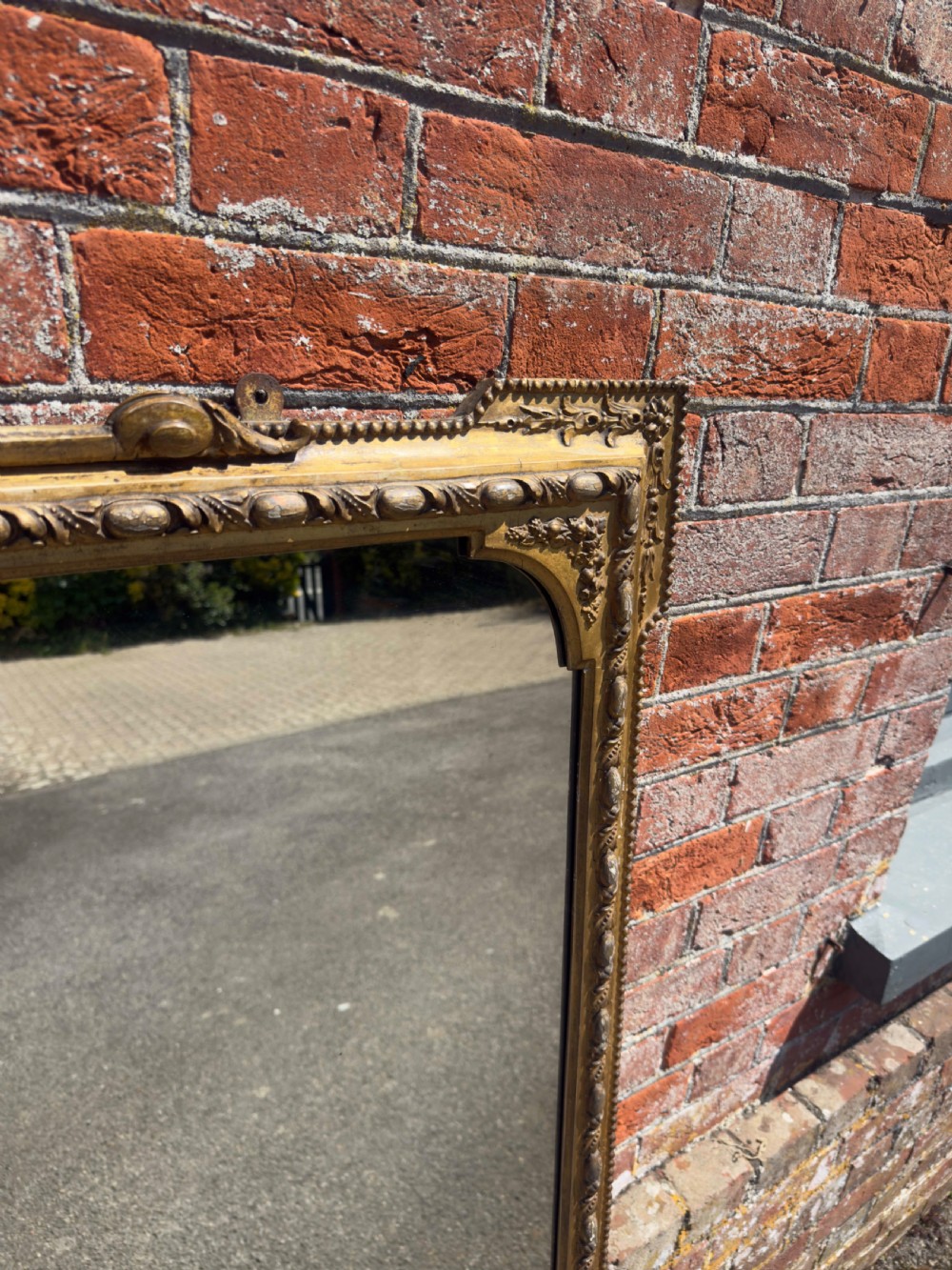 A large 19th-century English giltwood and gesso overmantel mirror featuring an ornate carved central crest, moulded frame, and scrolled side feet. View VI