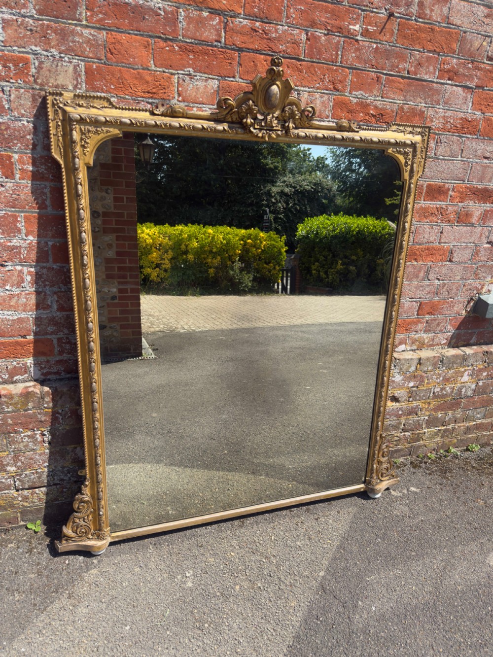 A large 19th-century English giltwood and gesso overmantel mirror featuring an ornate carved central crest, moulded frame, and scrolled side feet. View VII