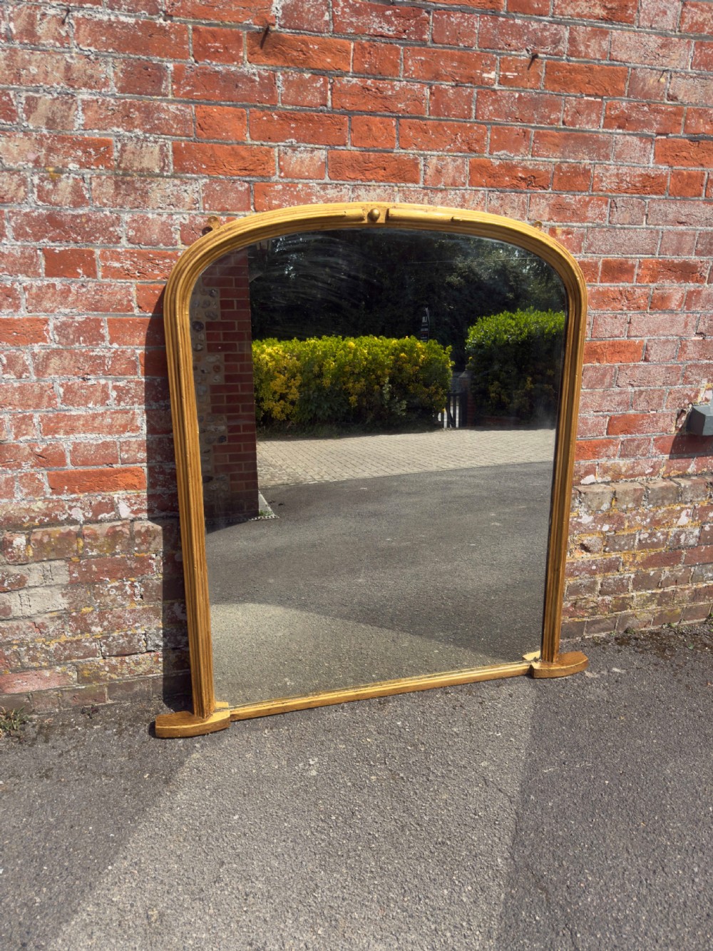 A 19th-century arched overmantel mirror featuring a gilded carved wood frame with integrated side support feet.