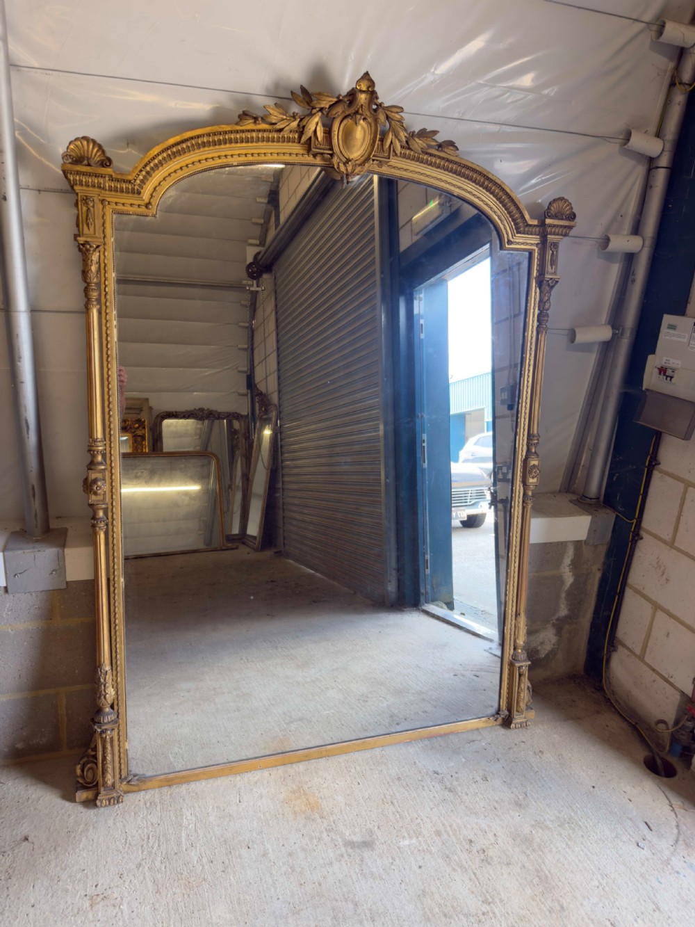 A large 19th-century gilded overmantel mirror featuring an arched top, carved crest with foliage, and decorative pilaster sides.