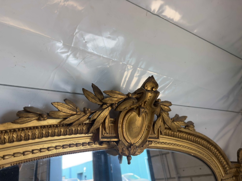 A large 19th-century gilded overmantel mirror featuring an arched top, carved crest with foliage, and decorative pilaster sides. View II