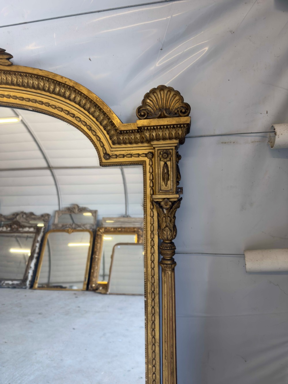 A large 19th-century gilded overmantel mirror featuring an arched top, carved crest with foliage, and decorative pilaster sides. View VI
