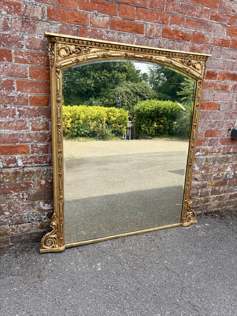 A large 19th-century Victorian arched giltwood and gesso overmantel mirror with ornamental mouldings and scrolled side brackets.