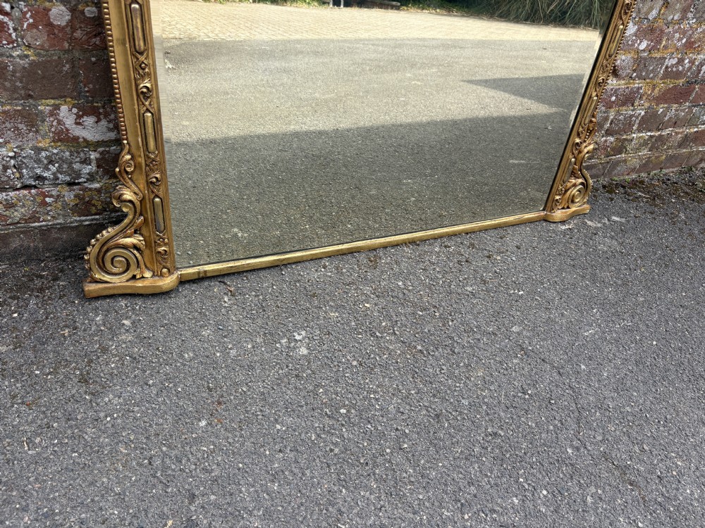 A large 19th-century Victorian arched giltwood and gesso overmantel mirror with ornamental mouldings and scrolled side brackets. View IV