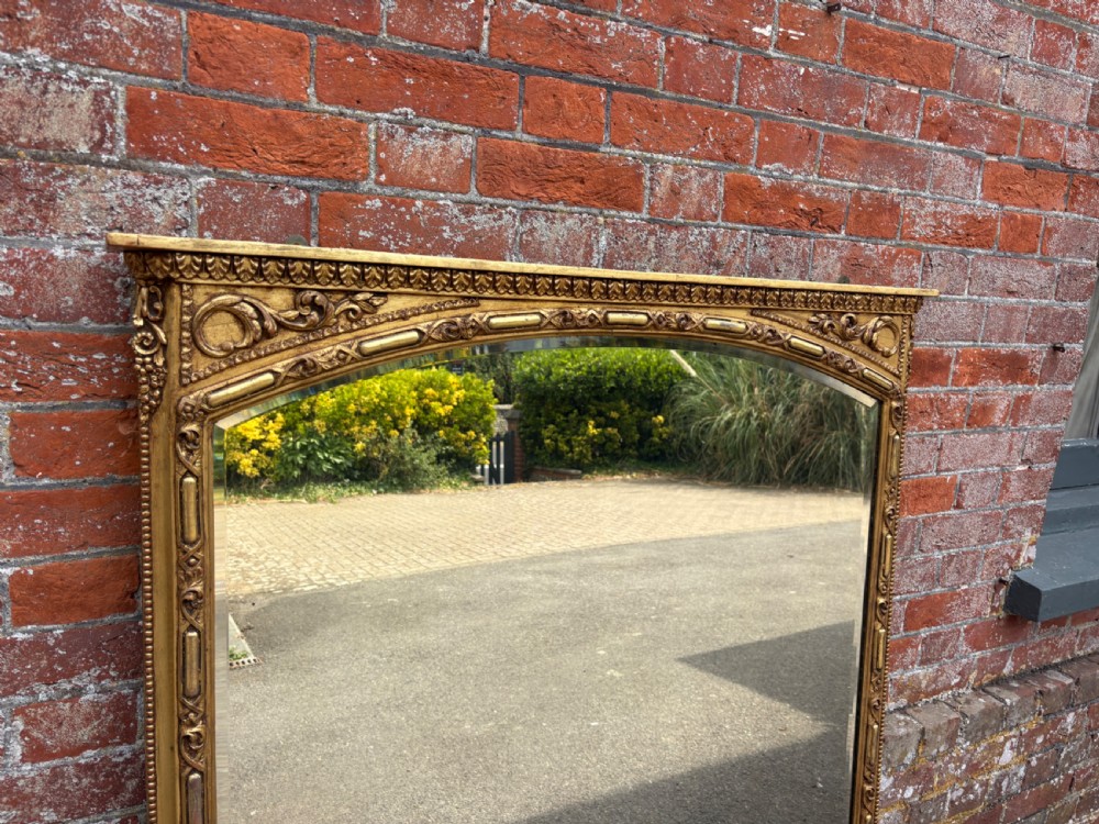 A large 19th-century Victorian arched giltwood and gesso overmantel mirror with ornamental mouldings and scrolled side brackets. View V
