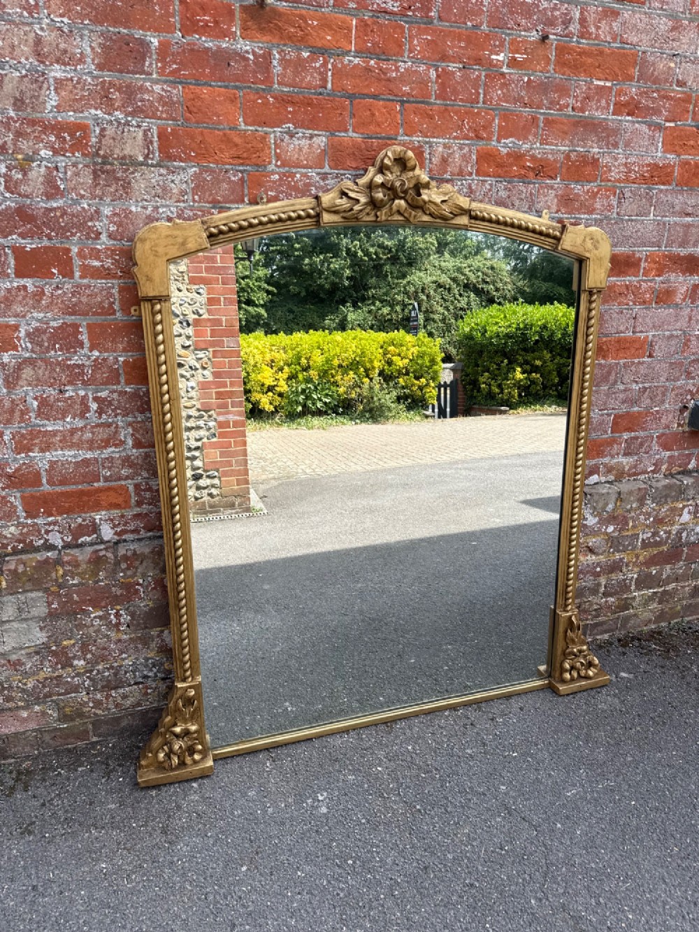 A large 19th-century overmantel mirror featuring a gilded wood frame with a central floral crest, rope-twist side columns, and an arched top.