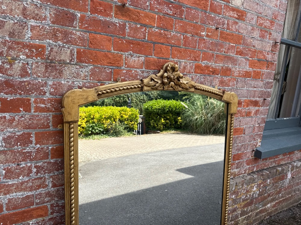 A large 19th-century overmantel mirror featuring a gilded wood frame with a central floral crest, rope-twist side columns, and an arched top. View IV