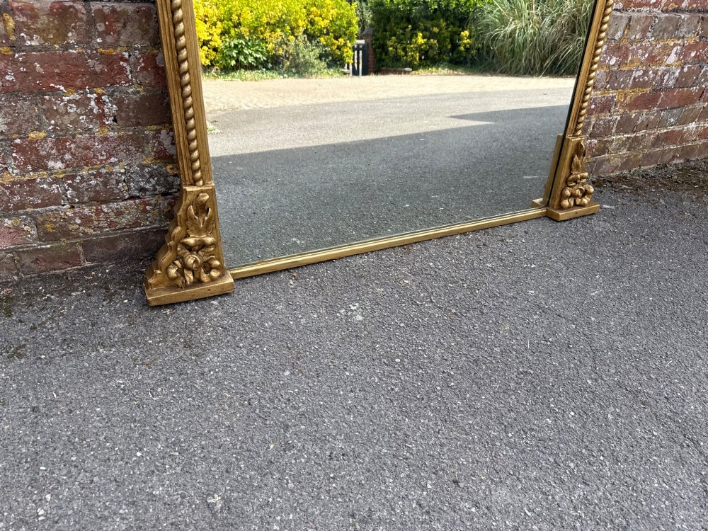 A large 19th-century overmantel mirror featuring a gilded wood frame with a central floral crest, rope-twist side columns, and an arched top. View V