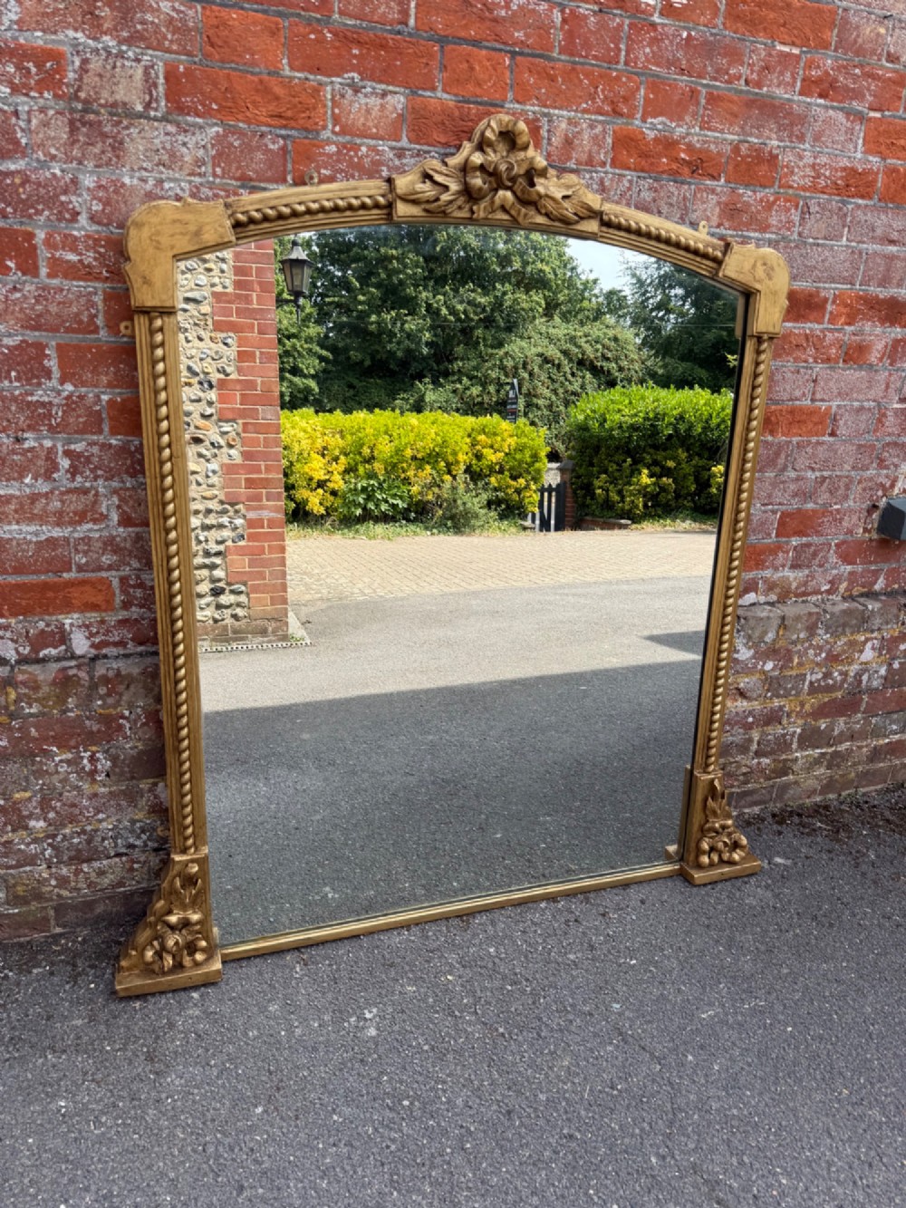 A large 19th-century overmantel mirror featuring a gilded wood frame with a central floral crest, rope-twist side columns, and an arched top. View VIII