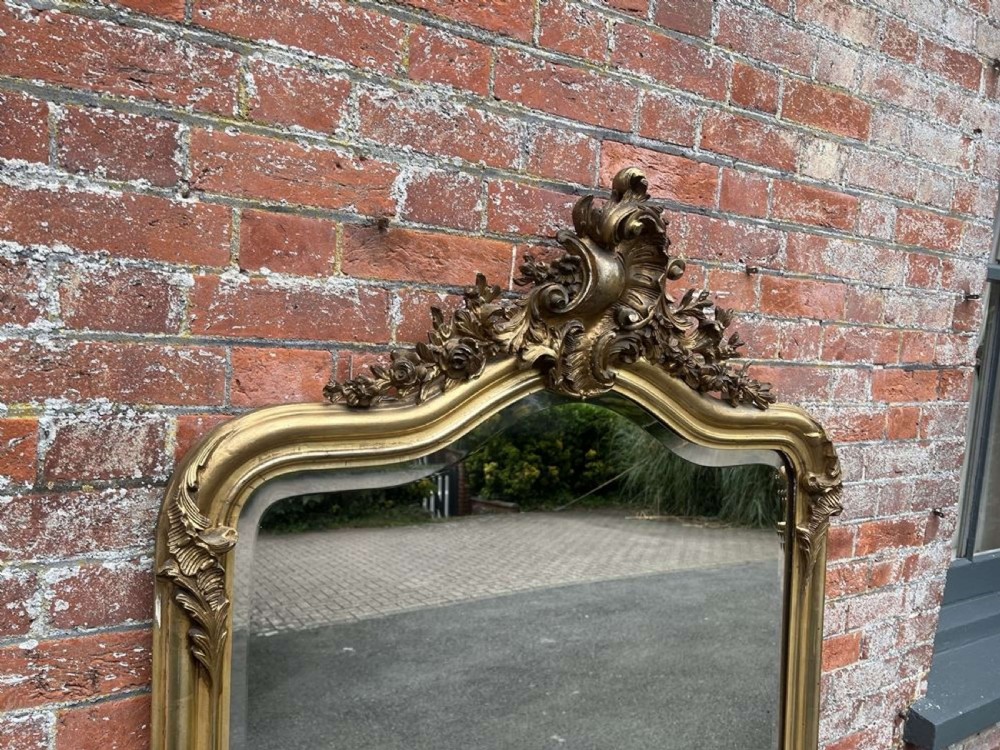 A 19th-century French giltwood overmantel mirror with an ornate shell cresting, floral scrollwork, and an arched top frame. View II