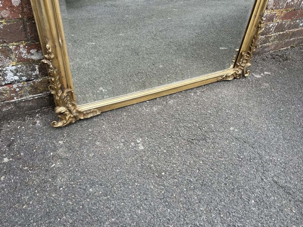 A 19th-century French giltwood overmantel mirror with an ornate shell cresting, floral scrollwork, and an arched top frame. View V