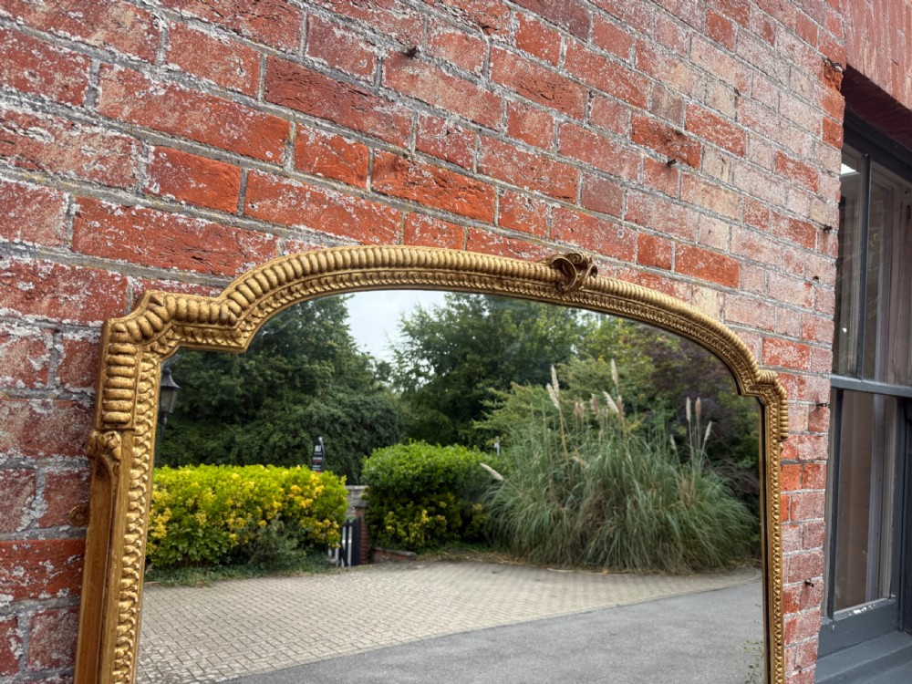 A large 19th-century gilded wood and gesso mirror with an arched top, ribbed frame, and decorative corner embellishments. View II