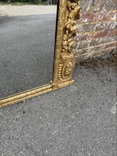 A large nineteenth-century carved giltwood overmantel mirror featuring a prominent central urn crest and floral mouldings. View VI