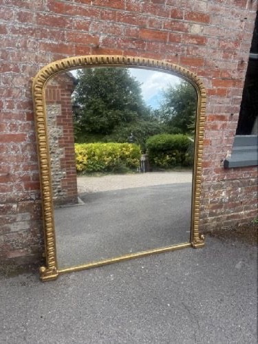 A large 19th-century overmantel mirror featuring an arched gold giltwood frame with fluted moulding detailing and a flat base.