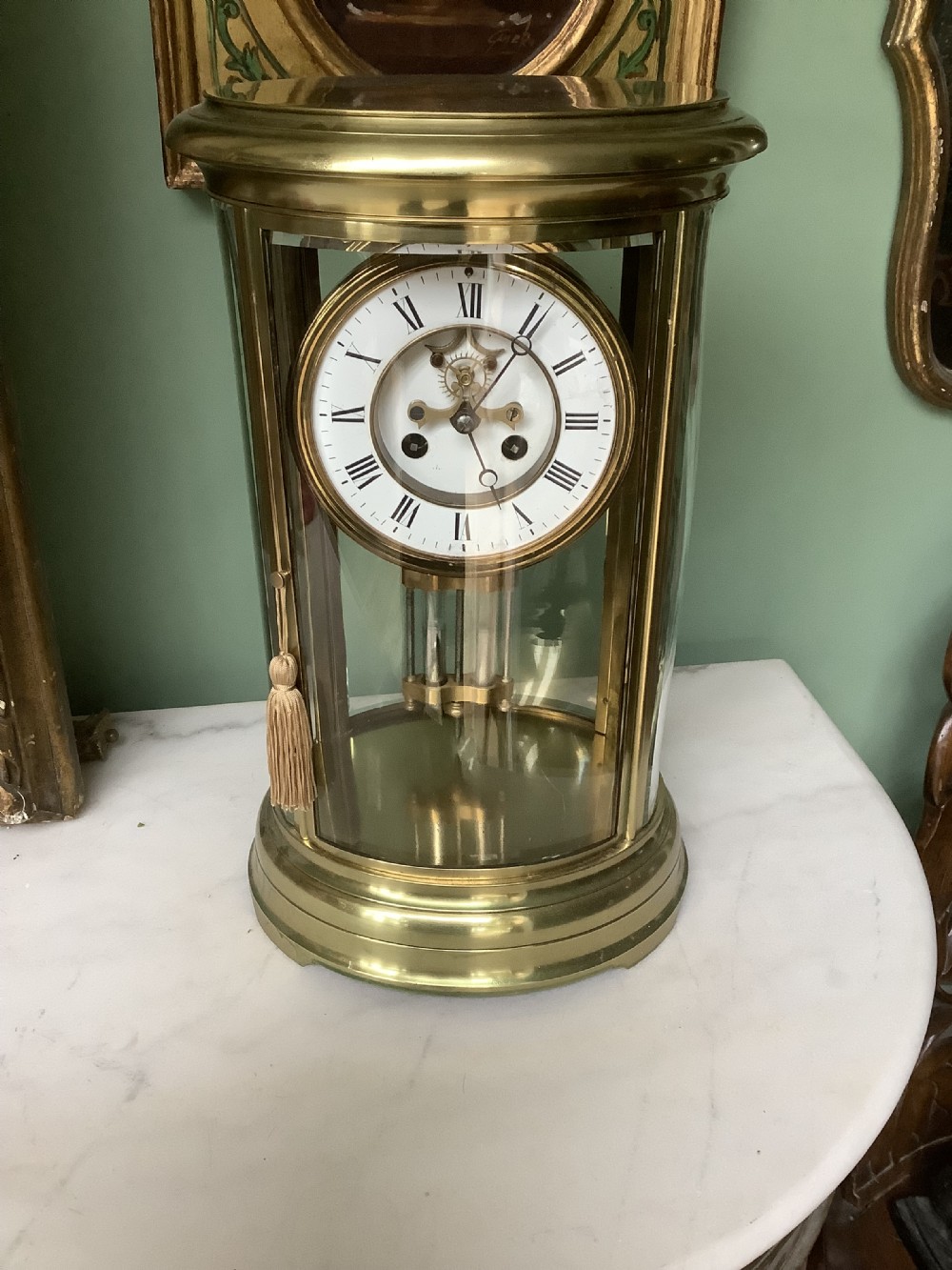 An oval brass and glass mantel clock with a white enamel dial showing Roman numerals and a visible mercury pendulum inside.