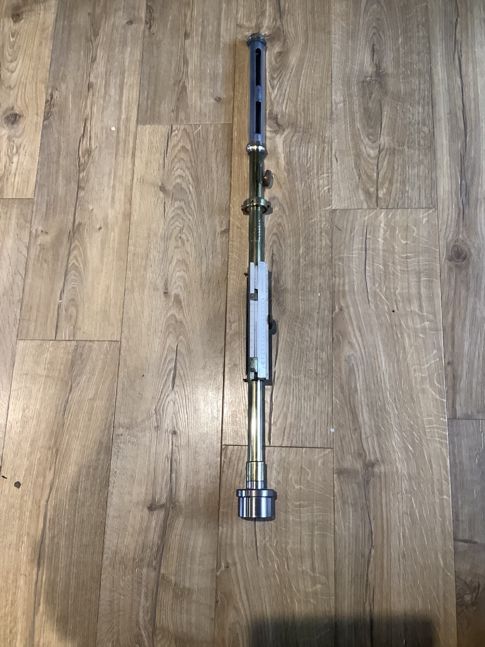A vertical brass marine stick barometer featuring a glass observation tube, silvered vernier scales, and a weighted cylindrical base.