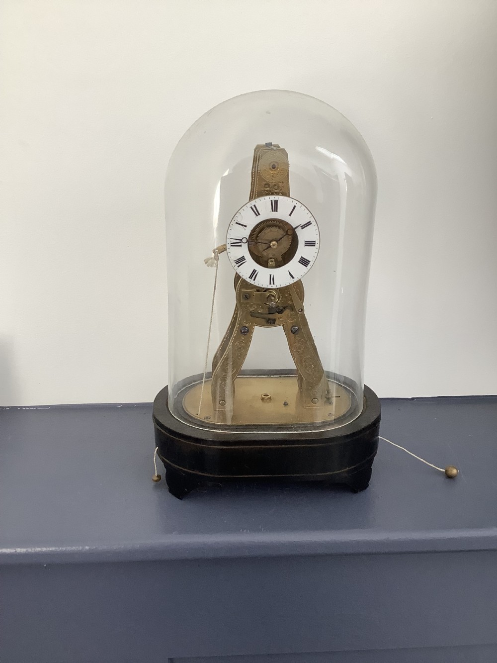 A Victorian brass skeleton clock featuring exposed internal gearing and an enamel dial, housed under a clear glass dome on a black wooden base.