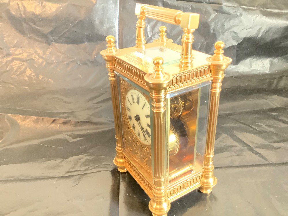 An ornate nineteenth-century French gilt brass carriage clock featuring fluted corner columns, intricate leaf scrollwork, a white enamel dial with Roman numerals, and a hinged top handle. View III
