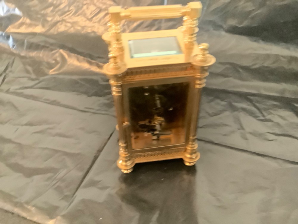 An ornate nineteenth-century French gilt brass carriage clock featuring fluted corner columns, intricate leaf scrollwork, a white enamel dial with Roman numerals, and a hinged top handle. View VI