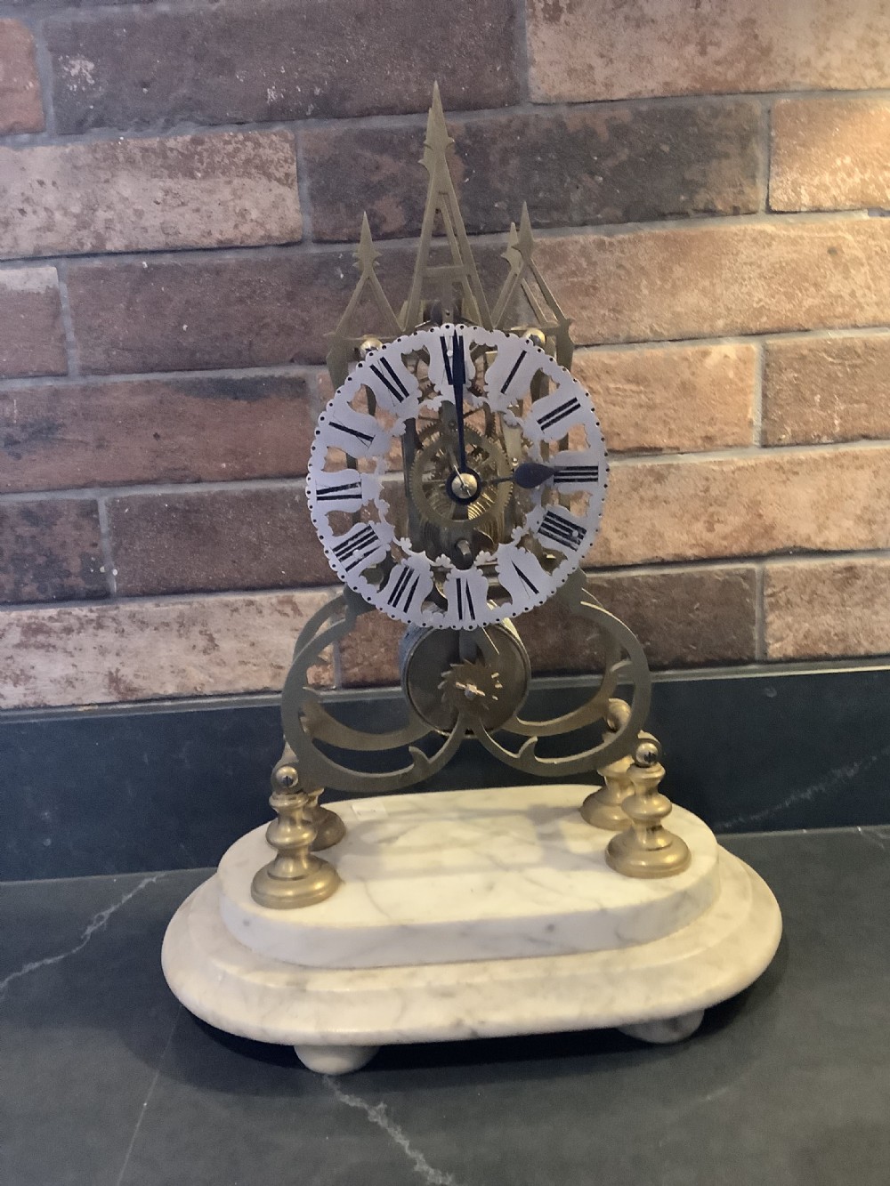 A Victorian brass skeleton clock featuring gothic architectural spires and a pierced silvered dial mounted on an oval white marble base.