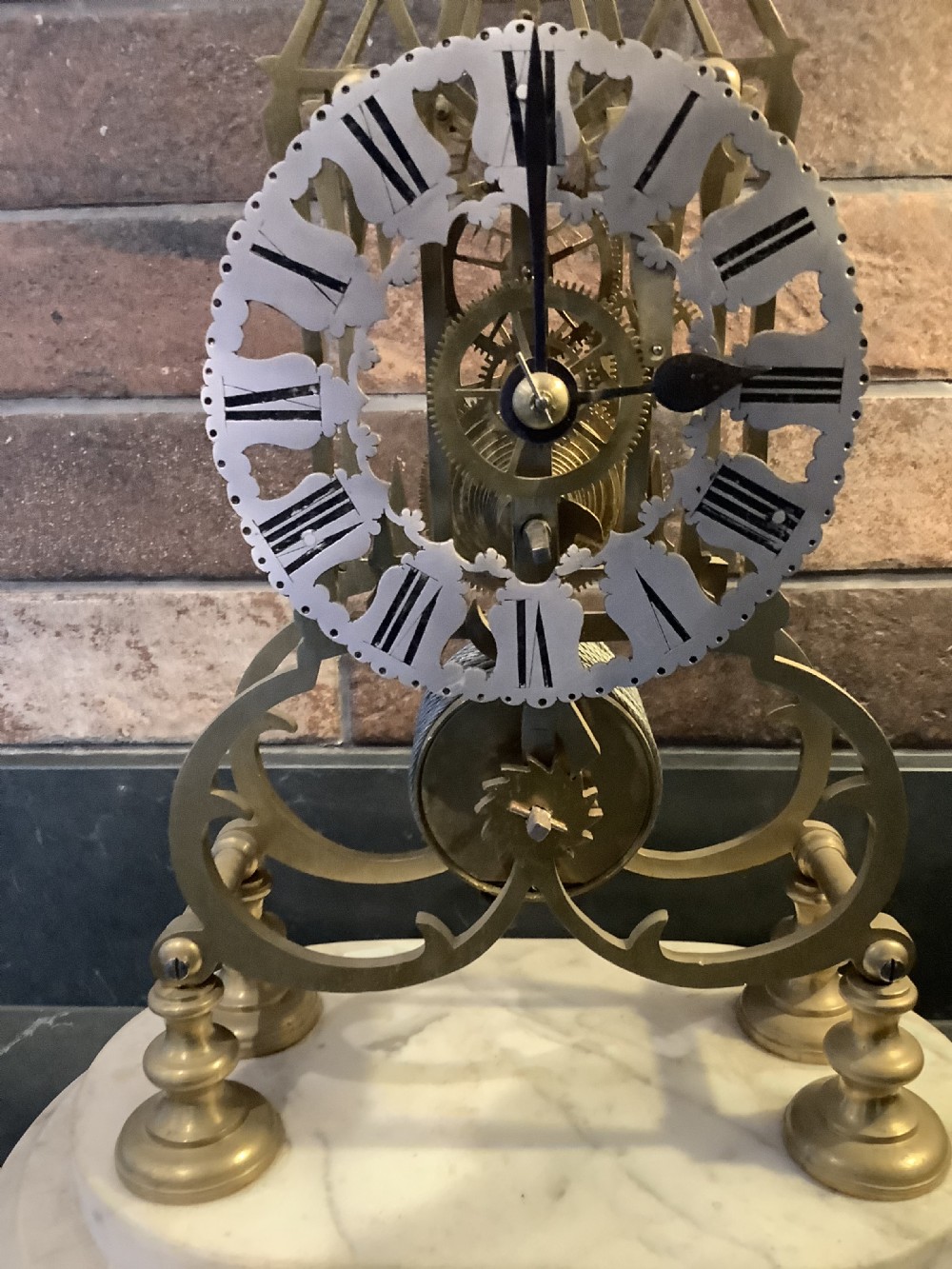 A Victorian brass skeleton clock featuring gothic architectural spires and a pierced silvered dial mounted on an oval white marble base. View VIII