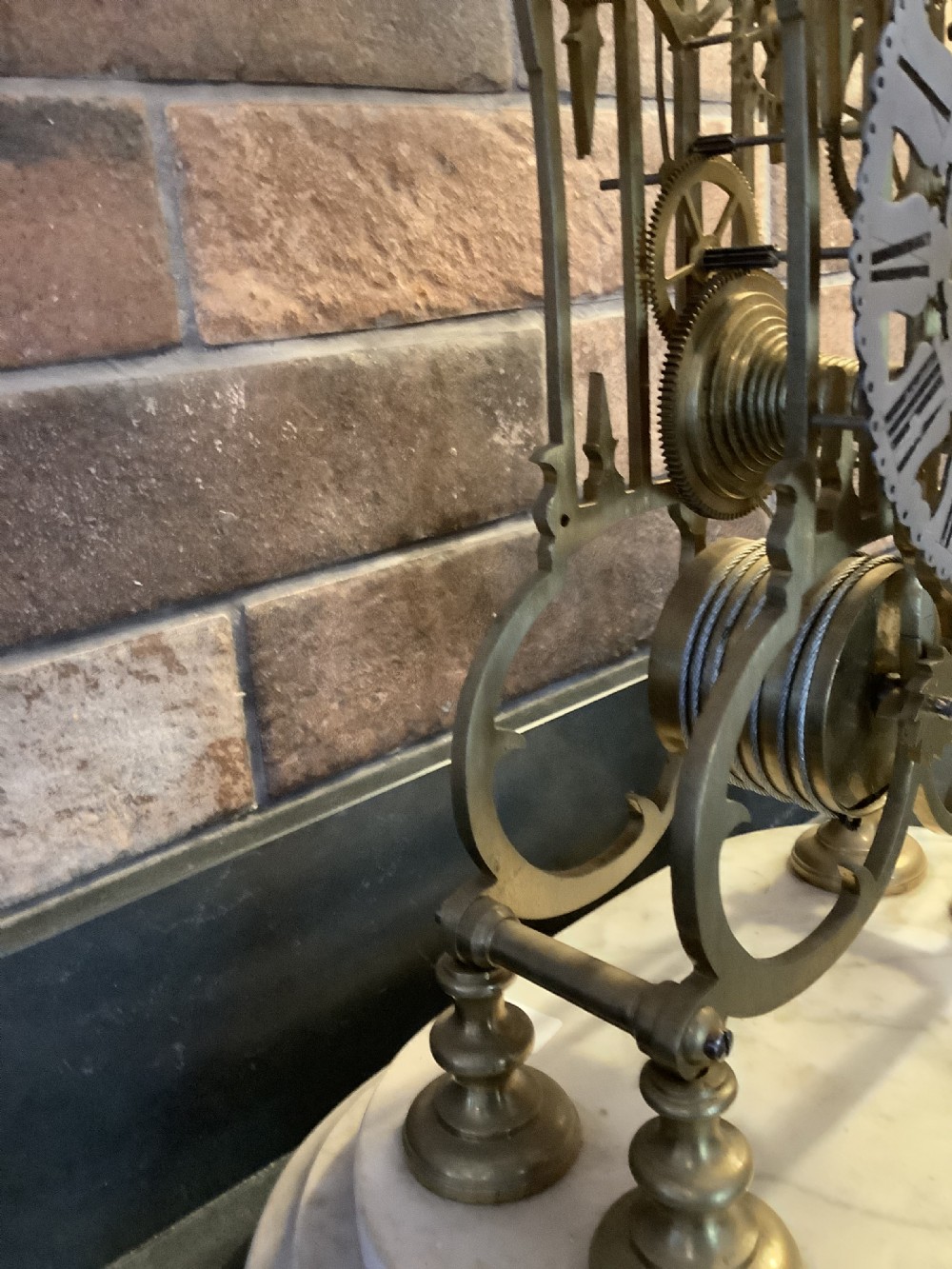 A Victorian brass skeleton clock featuring gothic architectural spires and a pierced silvered dial mounted on an oval white marble base. View IX