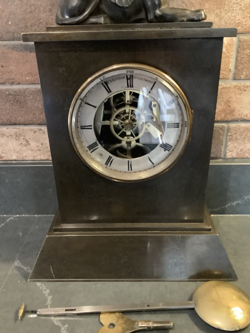A Victorian patinated bronze mantel clock featuring an open skeleton dial signed Frodsham Gracechurch Street alongside a brass pendulum and winding key.