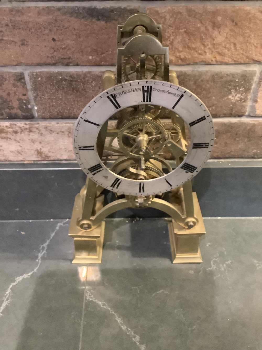 A Victorian patinated bronze mantel clock featuring an open skeleton dial signed Frodsham Gracechurch Street alongside a brass pendulum and winding key. View XII