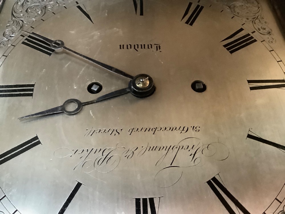 An antique arched ebonised wood bracket clock featuring brass pineapple finials, brass inlay, and an engraved metal dial with Roman numerals. View IX