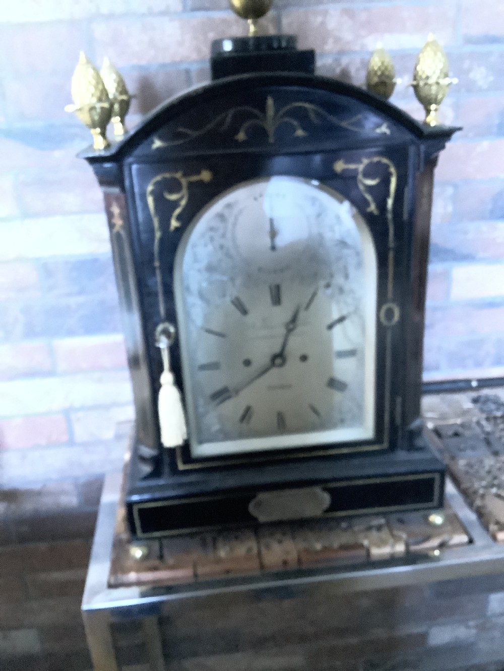 An antique arched ebonised wood bracket clock featuring brass pineapple finials, brass inlay, and an engraved metal dial with Roman numerals. View XIII