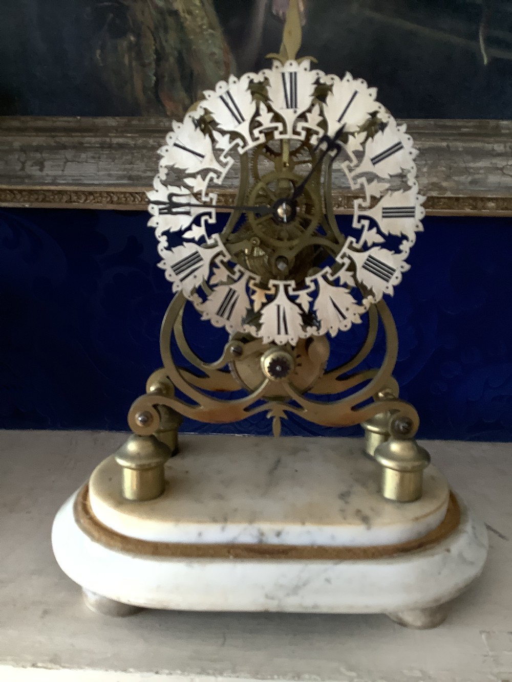A Victorian brass skeleton clock featuring an openwork frame, pierced chapter ring with Roman numerals, and a white marble plinth base.