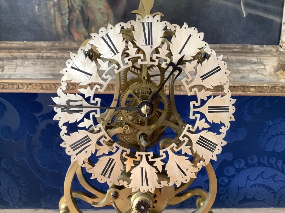 A Victorian brass skeleton clock featuring an openwork frame, pierced chapter ring with Roman numerals, and a white marble plinth base. View II