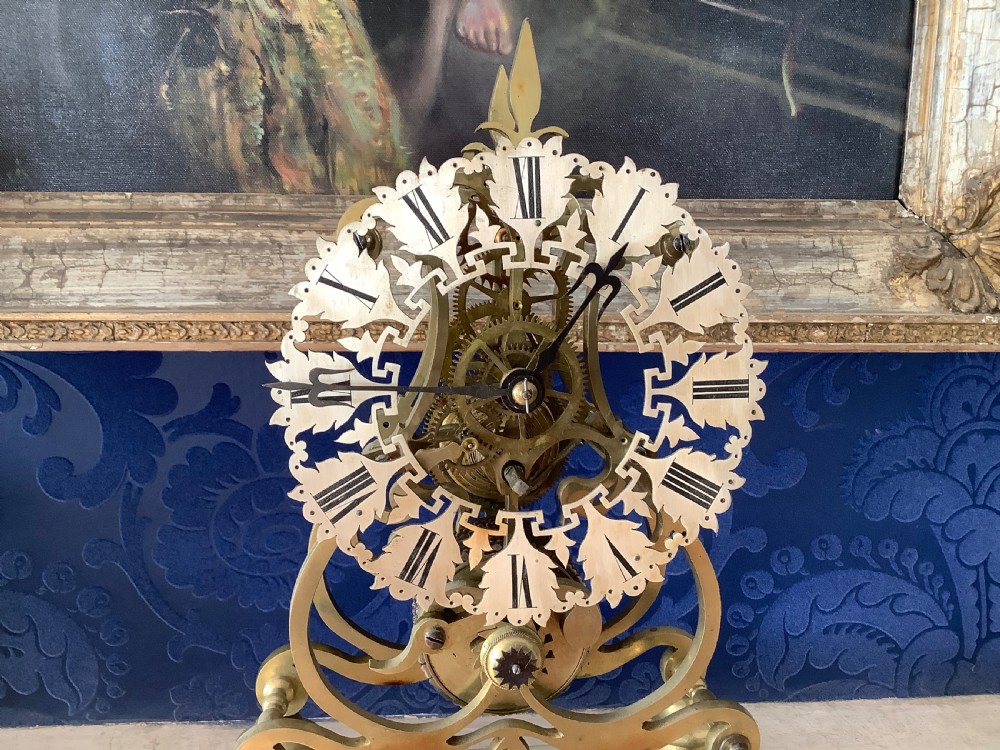 A Victorian brass skeleton clock featuring an openwork frame, pierced chapter ring with Roman numerals, and a white marble plinth base. View III