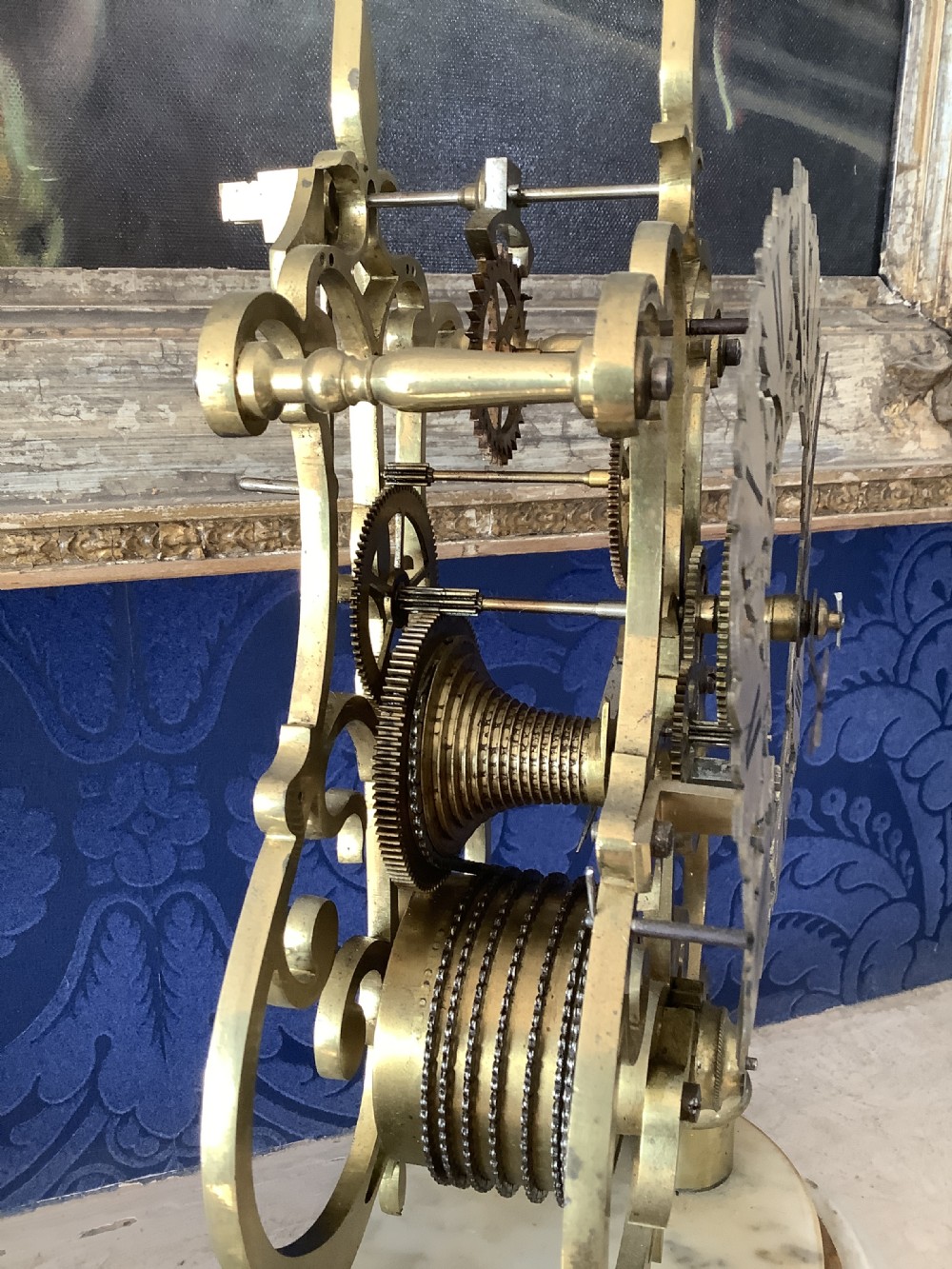 A Victorian brass skeleton clock featuring an openwork frame, pierced chapter ring with Roman numerals, and a white marble plinth base. View VII