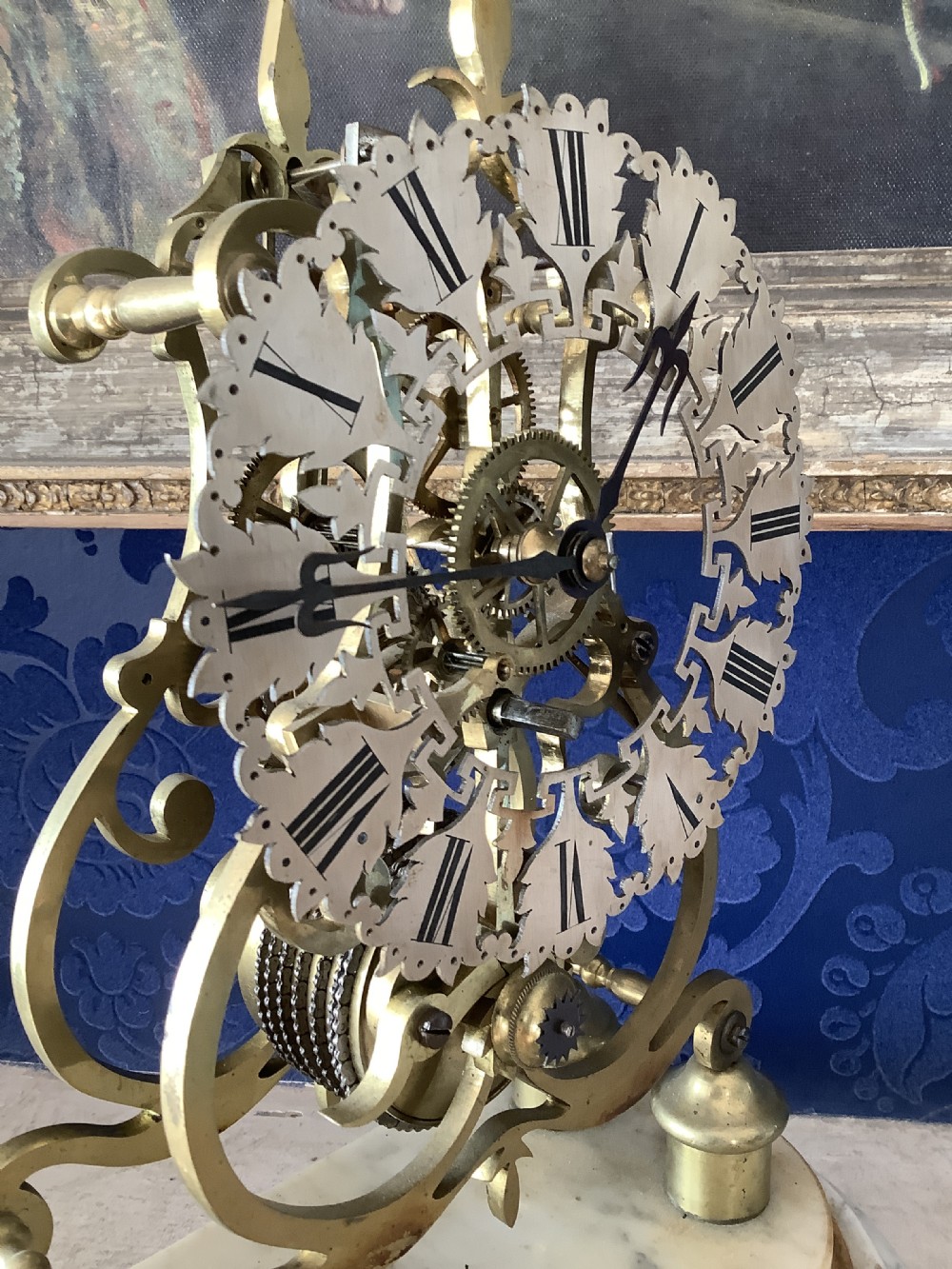 A Victorian brass skeleton clock featuring an openwork frame, pierced chapter ring with Roman numerals, and a white marble plinth base. View VIII