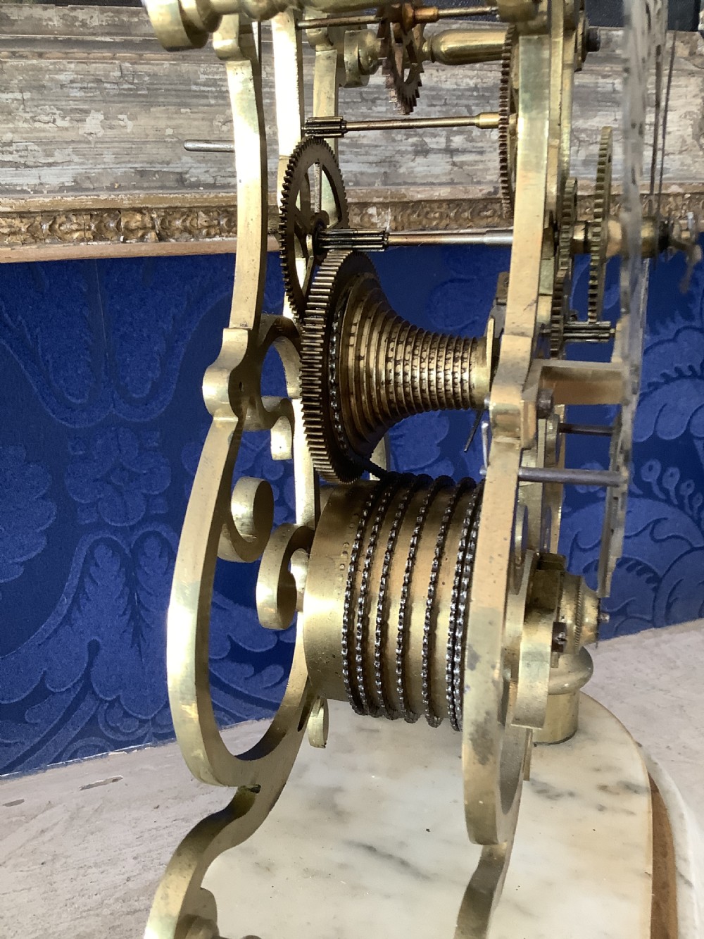A Victorian brass skeleton clock featuring an openwork frame, pierced chapter ring with Roman numerals, and a white marble plinth base. View IX