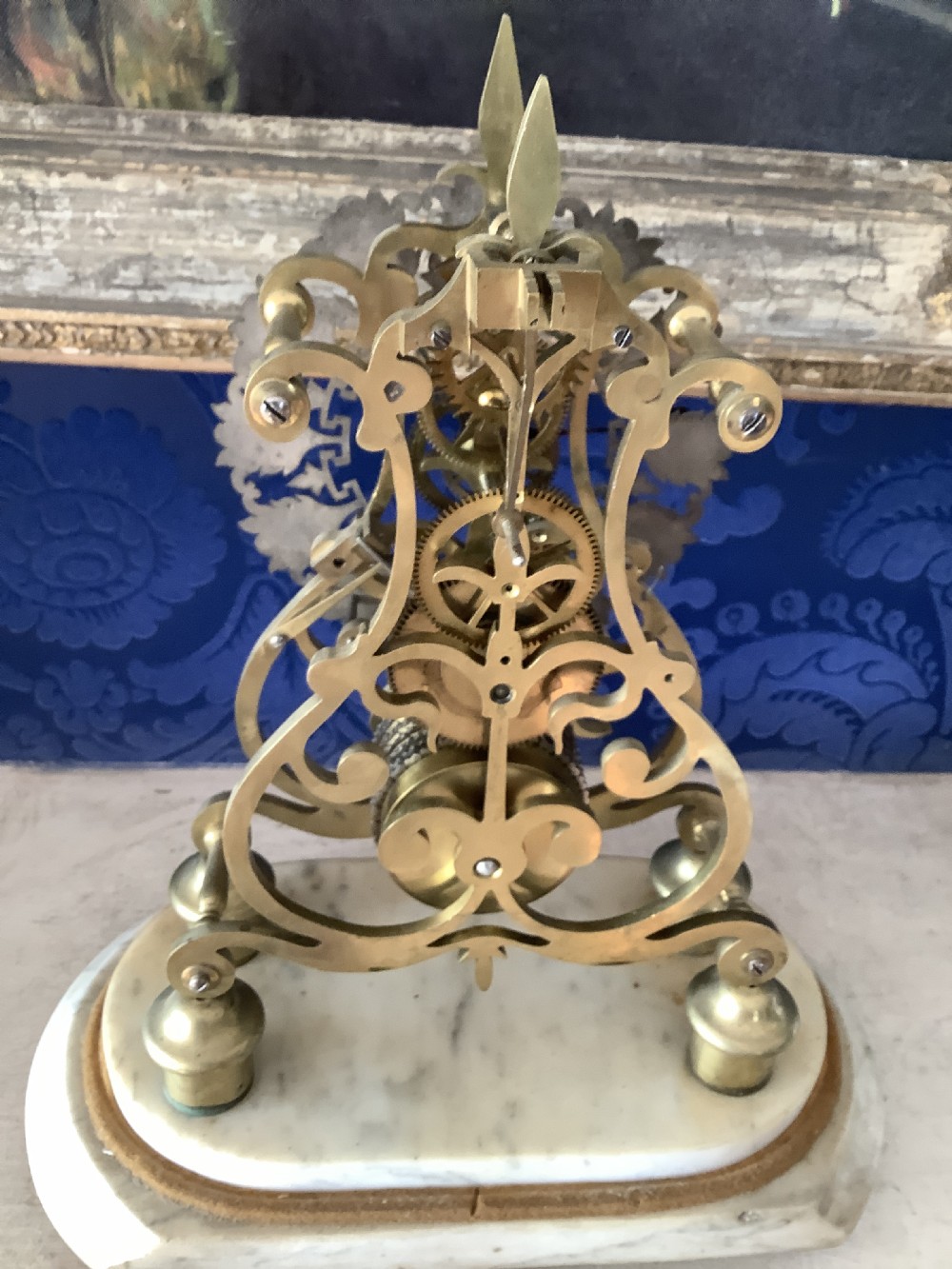 A Victorian brass skeleton clock featuring an openwork frame, pierced chapter ring with Roman numerals, and a white marble plinth base. View X